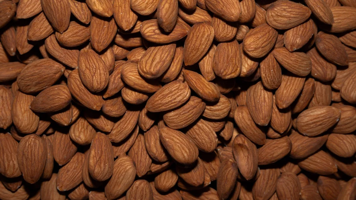 Trois sachets kraft d'amandes de formats différents posés sur un plan de travail à côté d'une balance de cuisine