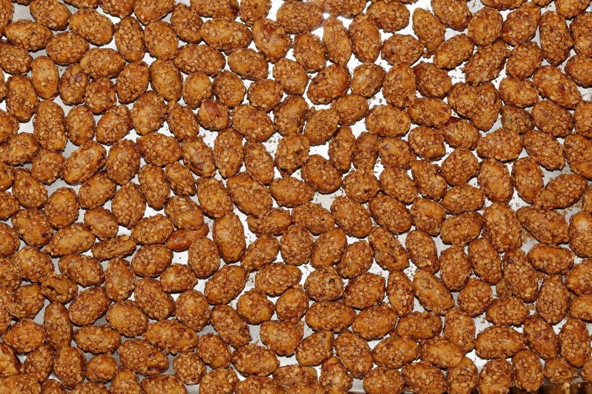 Amandes effilées en cours de torréfaction dans une poêle en fonte, remuées à la cuillère en bois sous une lumière chaude