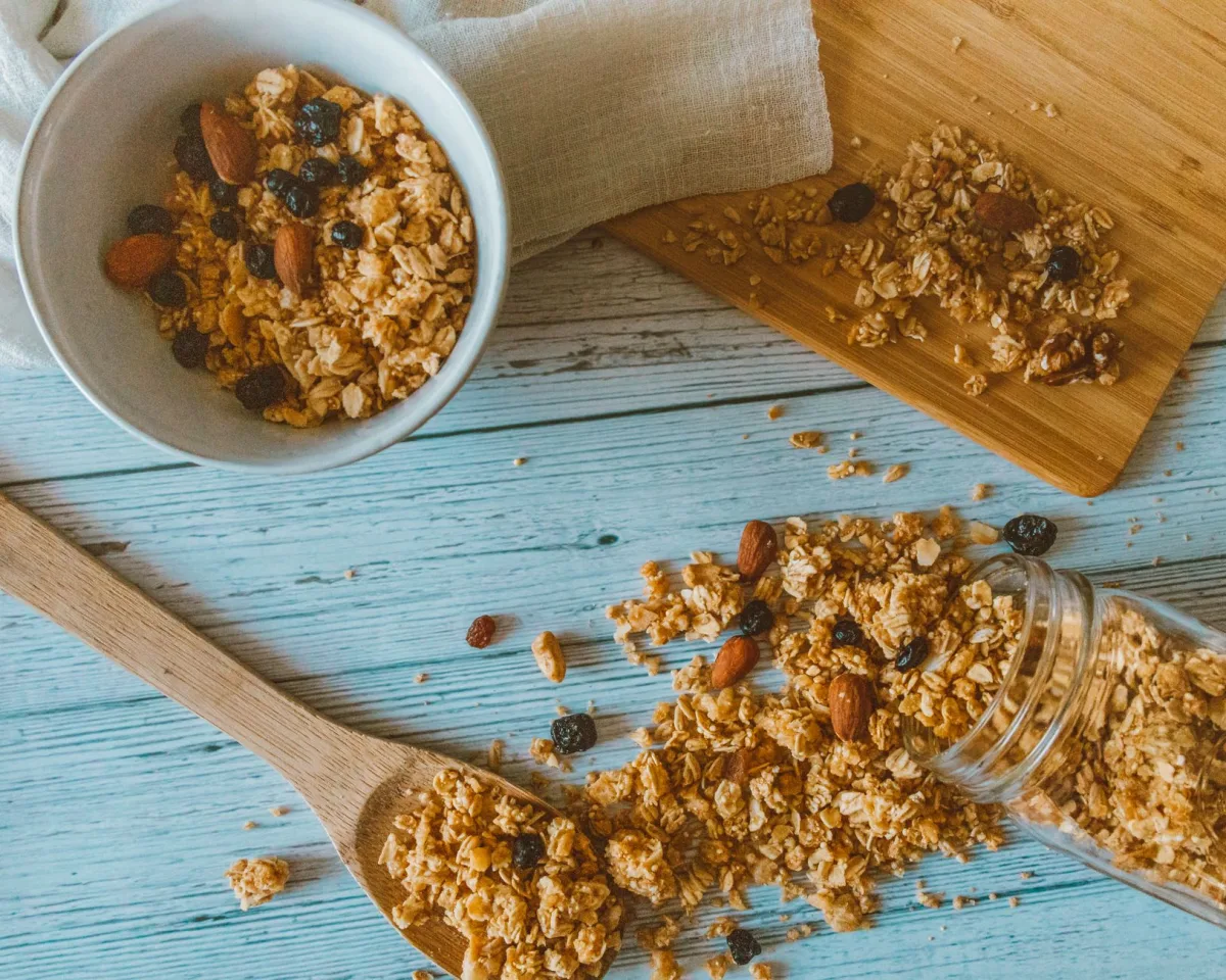 Trois bols de granola côte à côte sur une planche en bois, l'un aux fruits à coque, l'un nature, l'un au chocolat, lumière chaude latérale