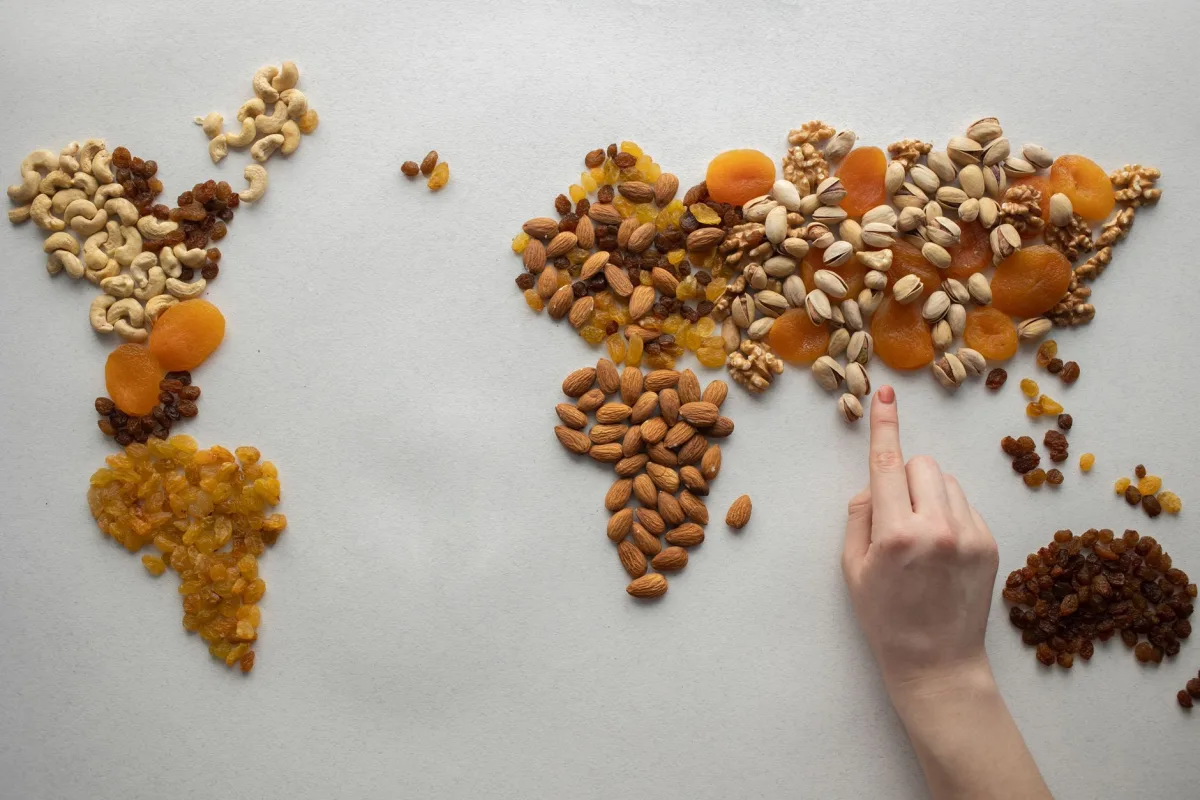 Quatre coupelles en céramique sur une planche en bois, contenant des pistaches, un mélange de fruits à coque, des raisins secs et des copeaux de fruits exotiques séchés