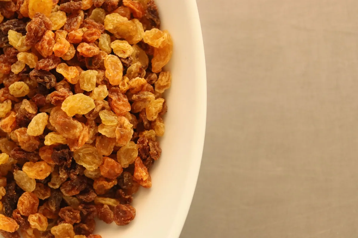 Trois coupelles en céramique contenant des raisins sultanines ambrés, des raisins de Corinthe noirs et des raisins muscat à gros grains