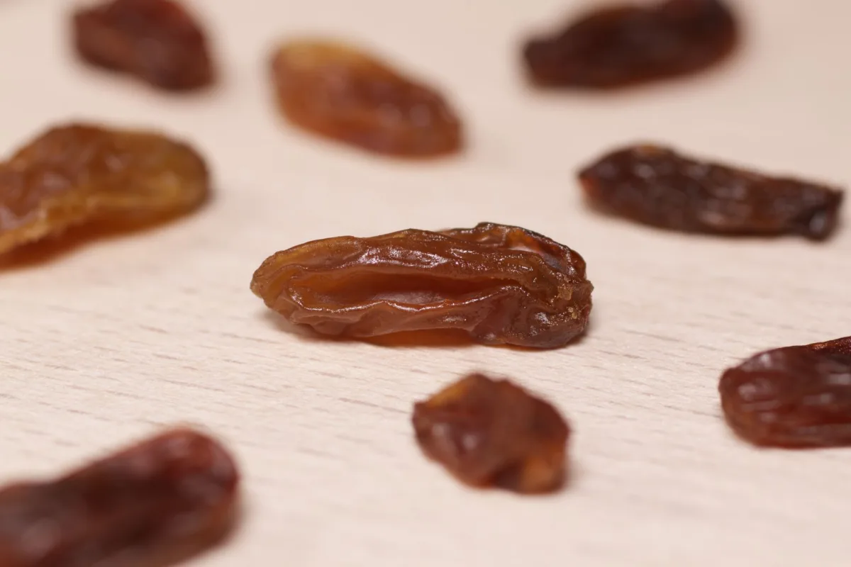 Mains tenant un sachet de raisins secs ouvert, liste d'ingrédients et tableau nutritionnel visibles au dos