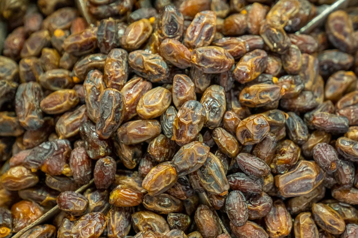 Trois sachets kraft ouverts de dattes, d'abricots secs et de raisins secs alignés sur une planche en bois