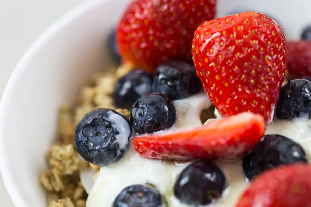 Bol de yaourt nature avec fruits rouges, granola et amandes concassées déposés en surface
